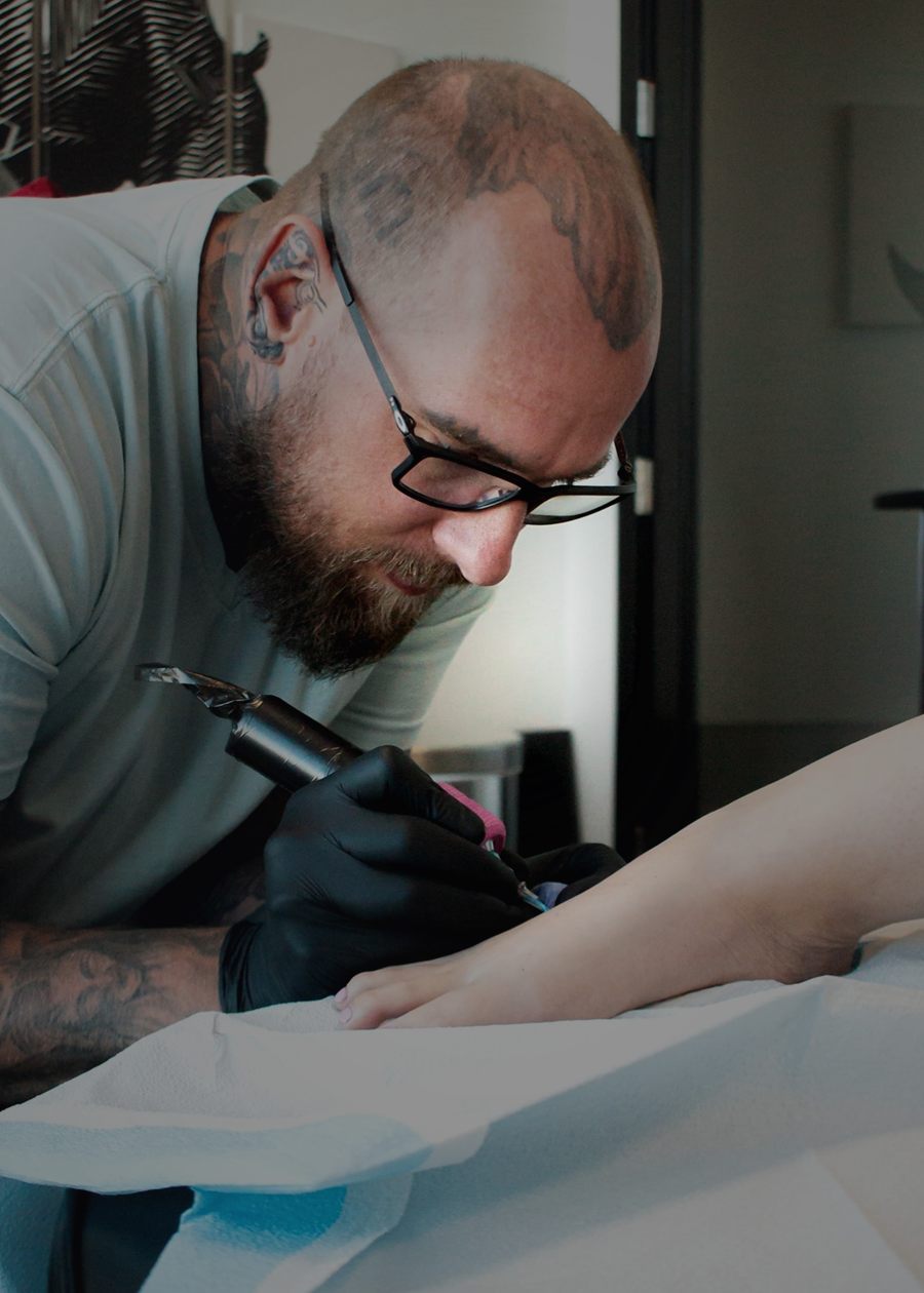 Ryan leaning in close while tattooing a client's forearm.