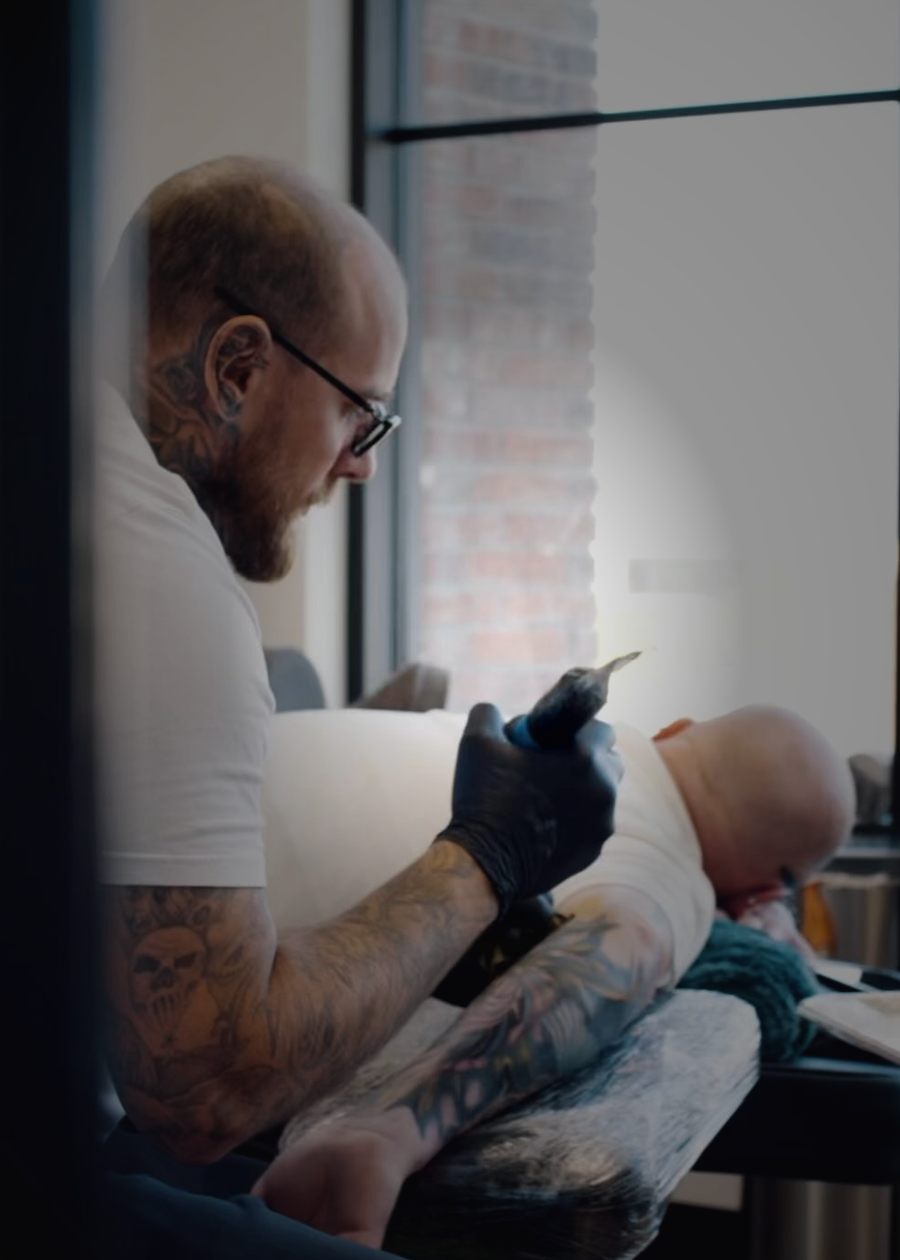 Ryan tattooing a client beside the studio window.