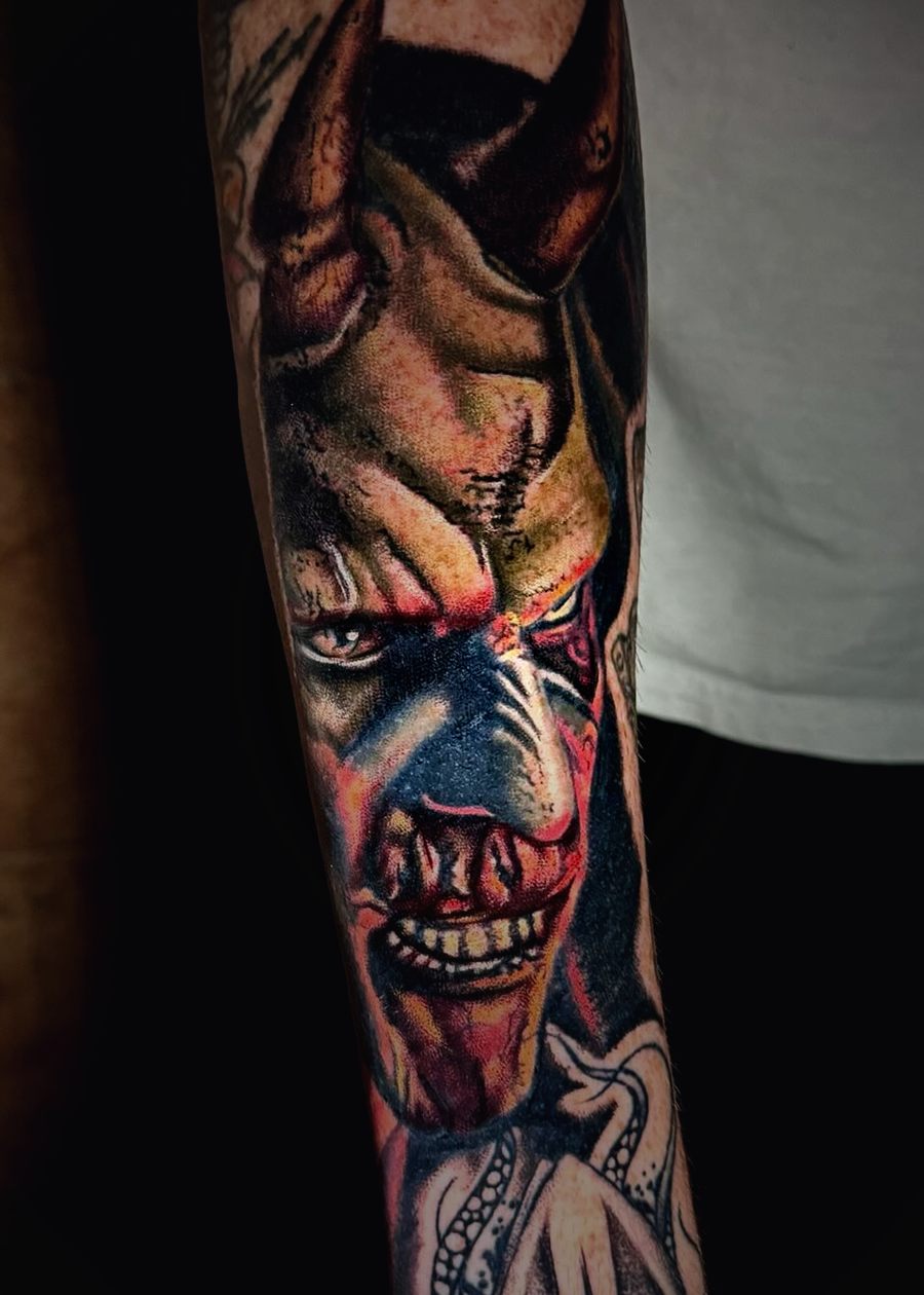 Color demon face with horns tattooed on a forearm.