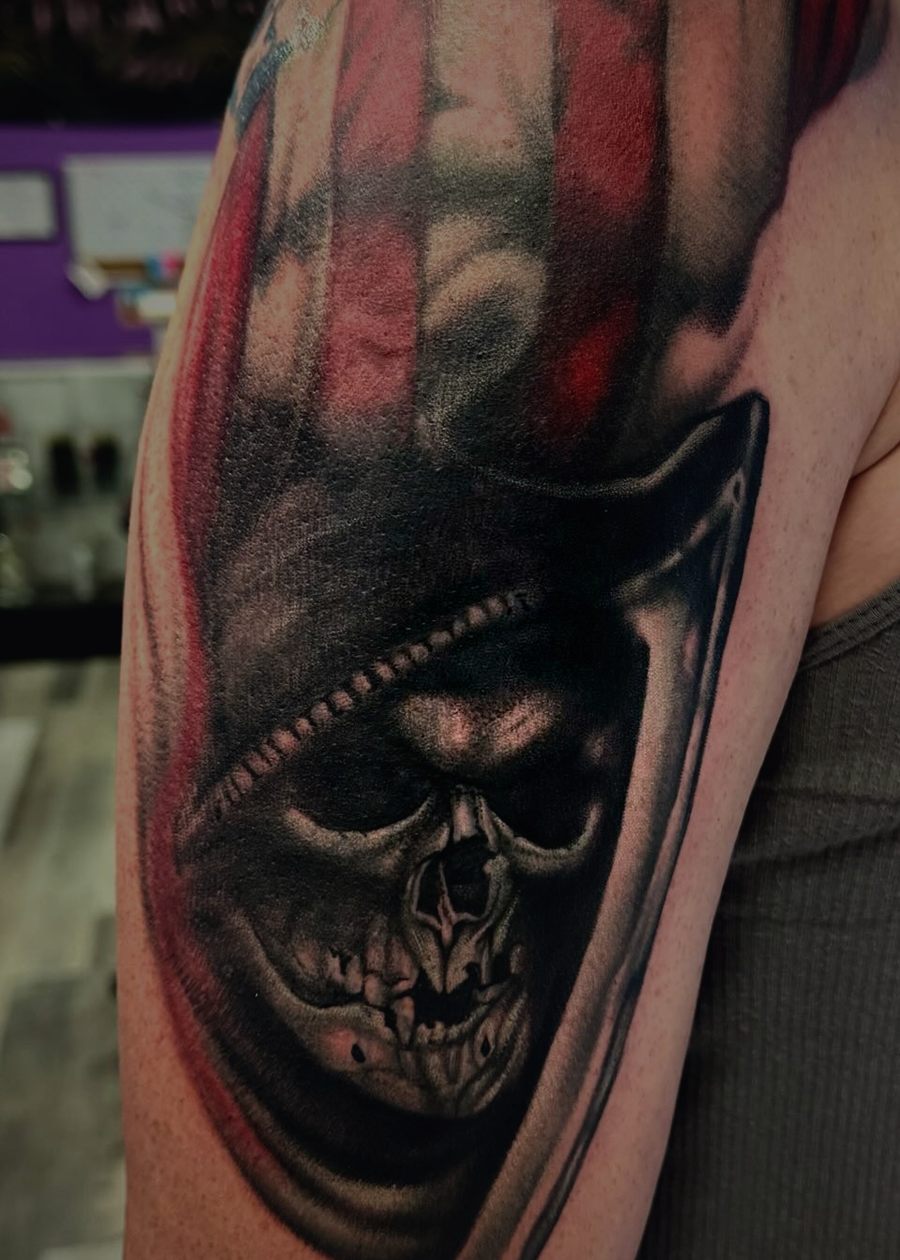 Black and grey reaper behind a torn flag, tattooed across a shoulder.