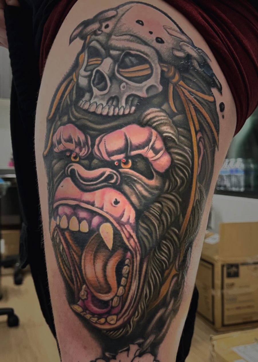 New school color gorilla wearing a skull headdress, tattooed on a thigh.