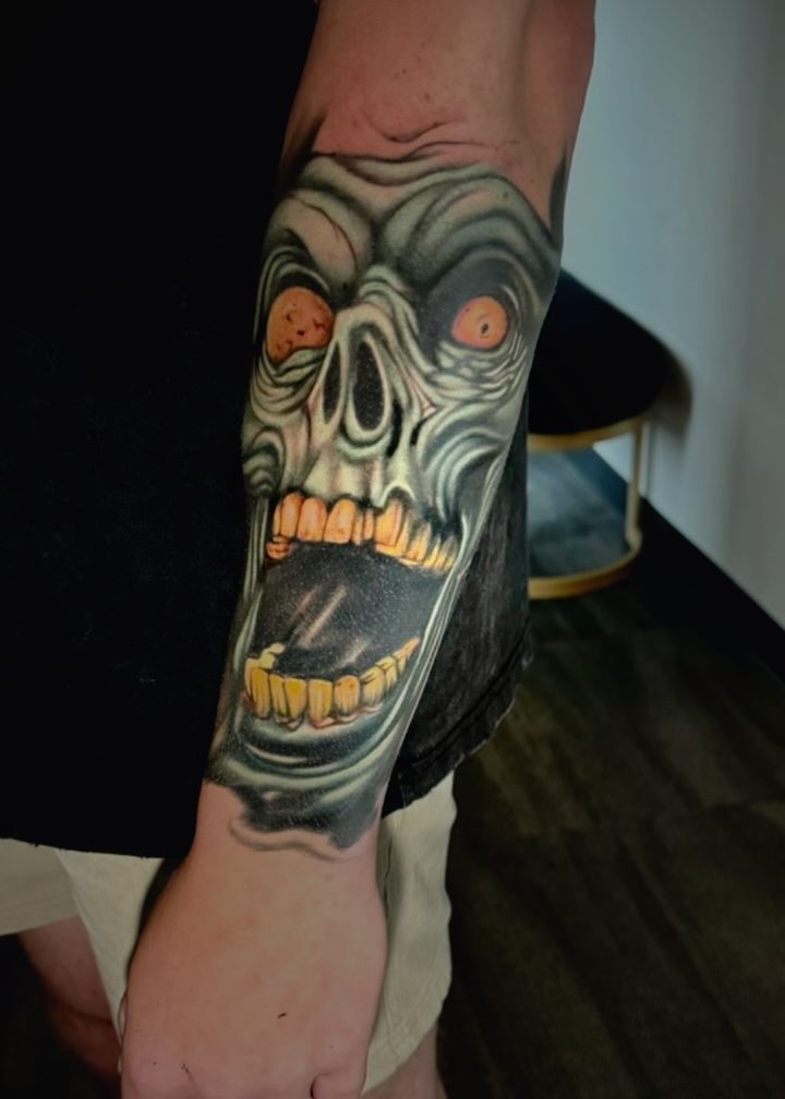 Color horror face with orange eyes and gold teeth wrapping a forearm.
