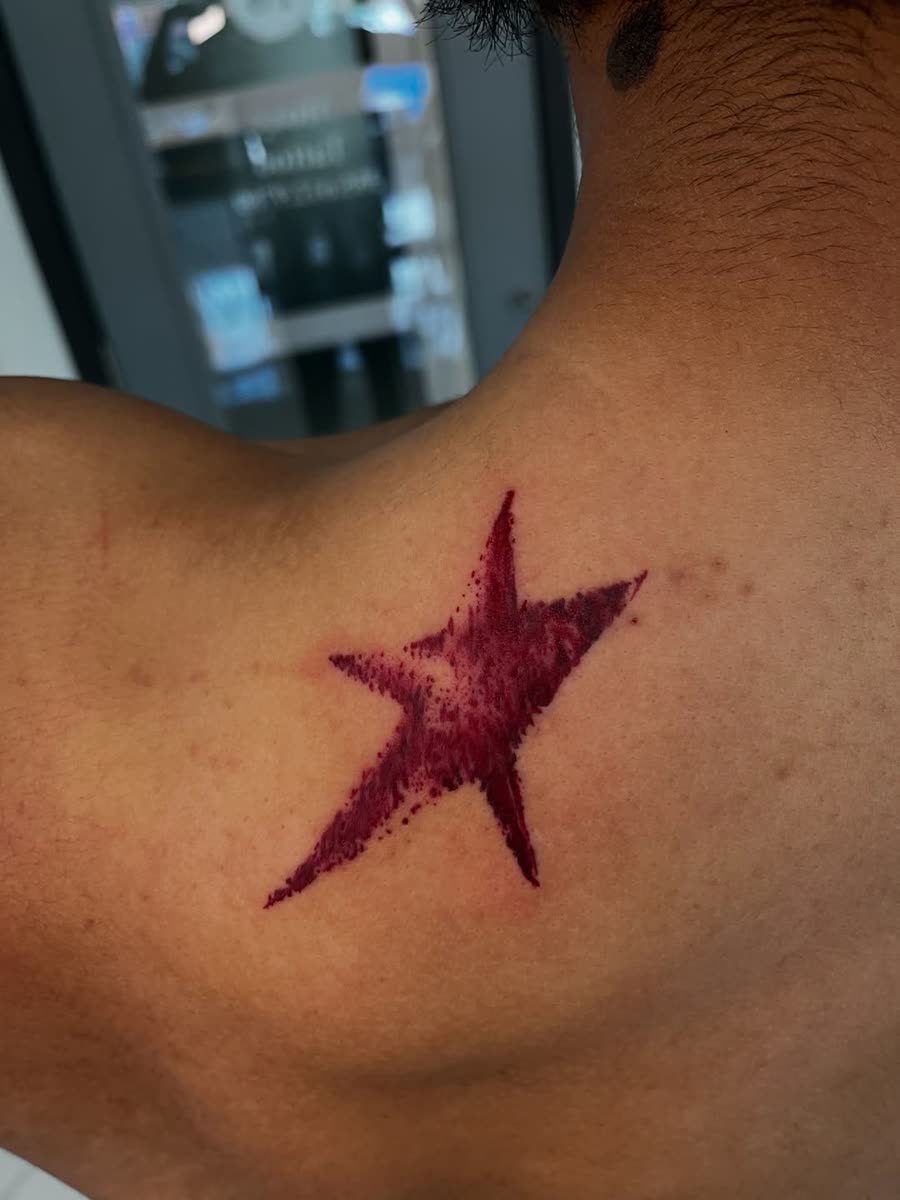 Solid red star tattooed on a shoulder blade.