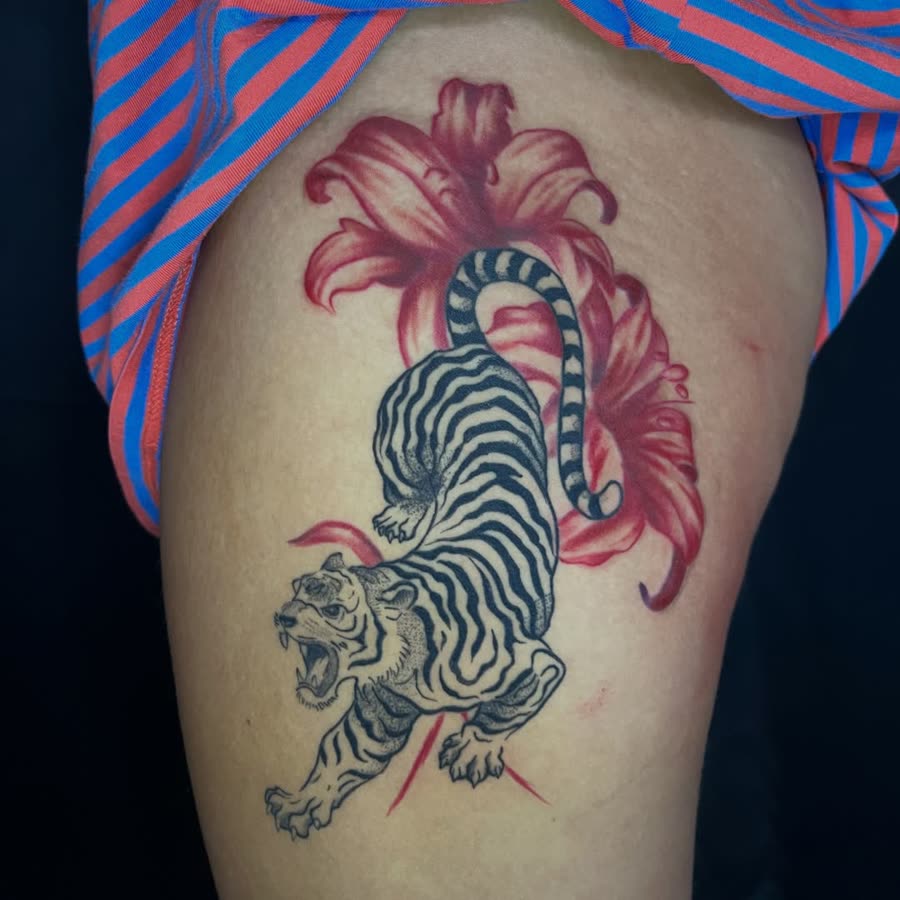 Traditional crawling tiger with red lilies tattooed on a thigh.