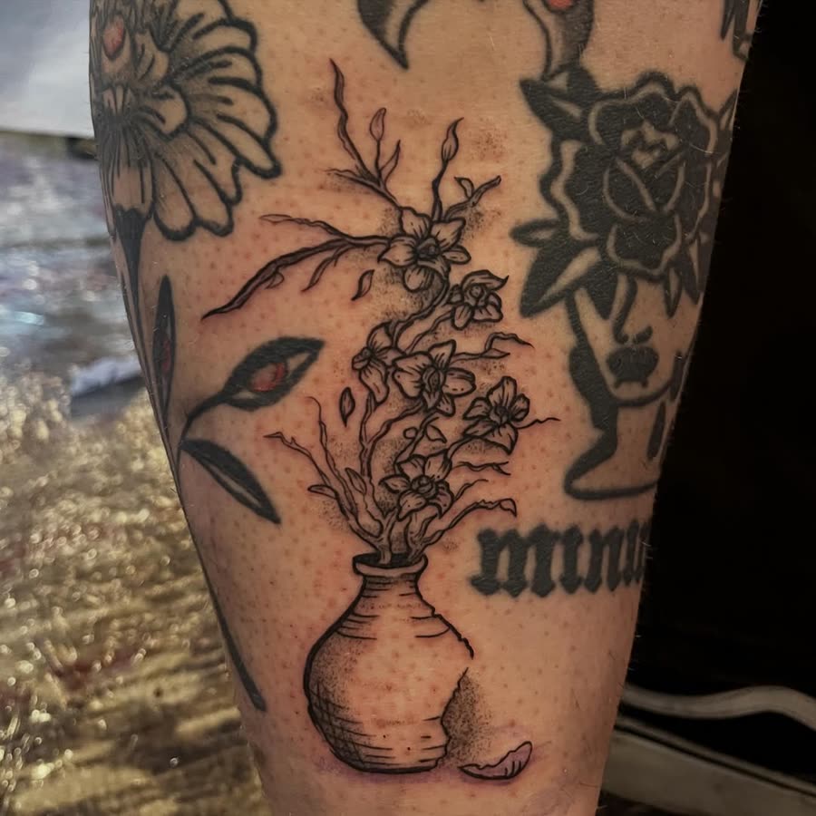 Fine line vase of flowers with lettering, tattooed on a calf.