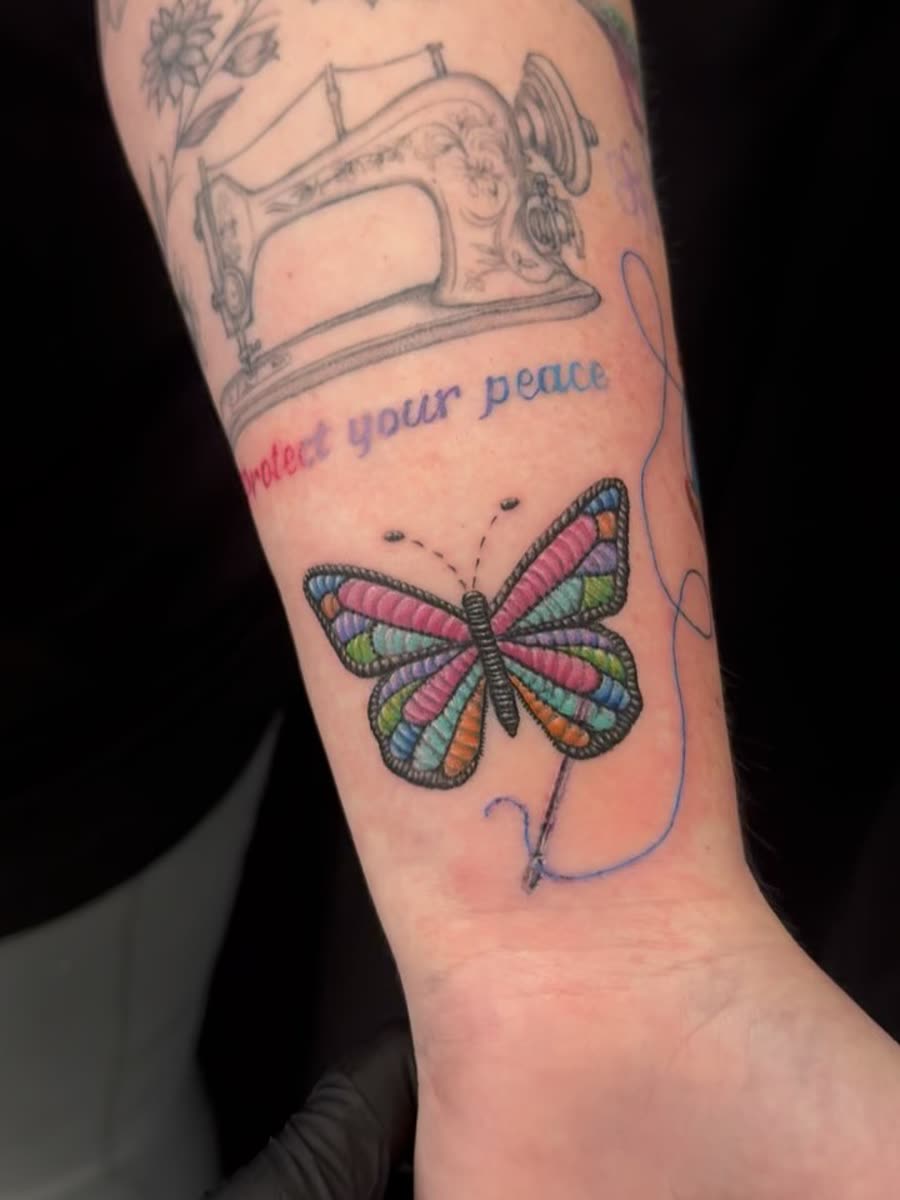 Colour butterfly with lettering tattooed above a knee.