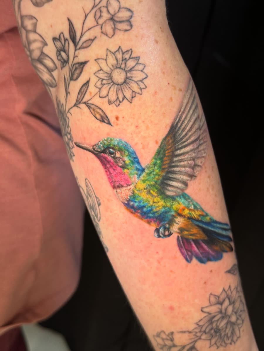 Colour hummingbird and flowers tattooed on an inner arm.