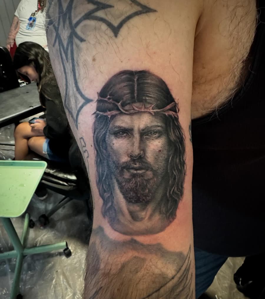 Black and grey portrait of Jesus tattooed on an upper arm.