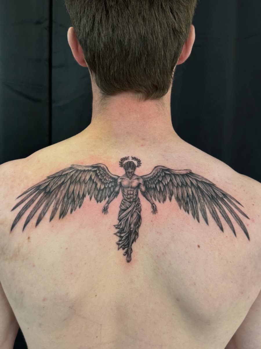 Fine line winged dagger tattooed across an upper back.