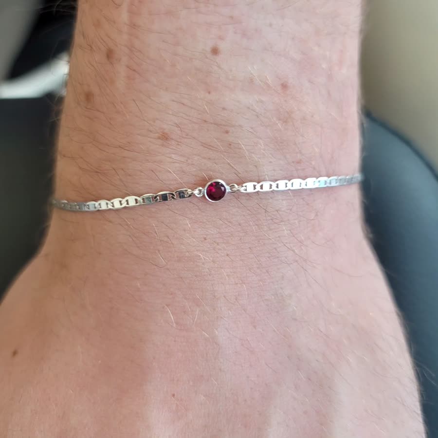 Fine silver permanent bracelet with a red birthstone, welded on a wrist.