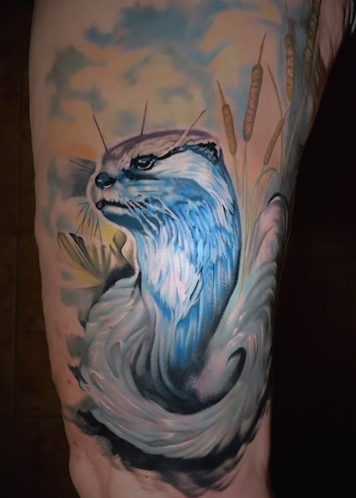 Watercolor style otter in water with cattails, tattooed on an upper arm.